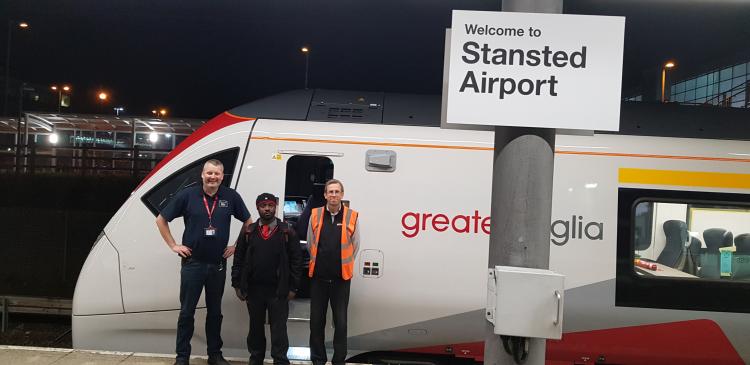 Three people standing next to a Greater Anglia train at Stansted Airport