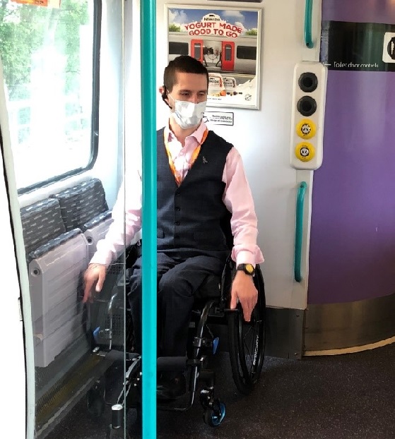 Man wearing a blue face covering sitting in wheelchair on a train