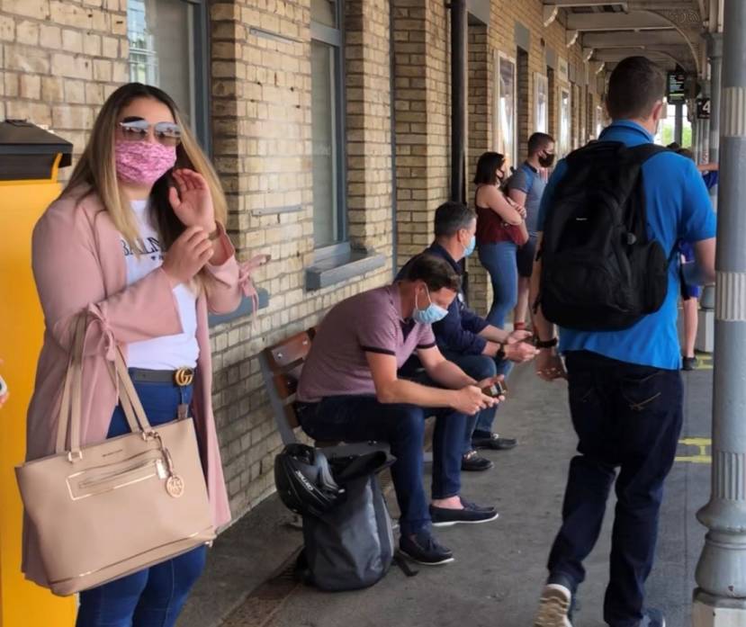 Passengers wearing face coverings waiting for a train on a platform