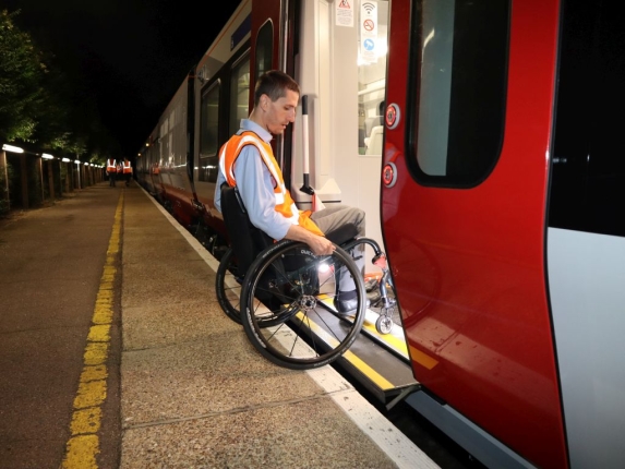 Man in a wheelchair wearing a high visibility jacket gets on train using the retractable step. 