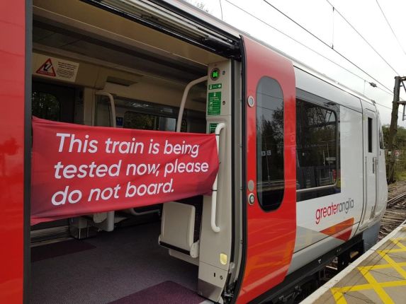 A train with open doors and a red banner saying 'this train is being tested now, please do not board.'