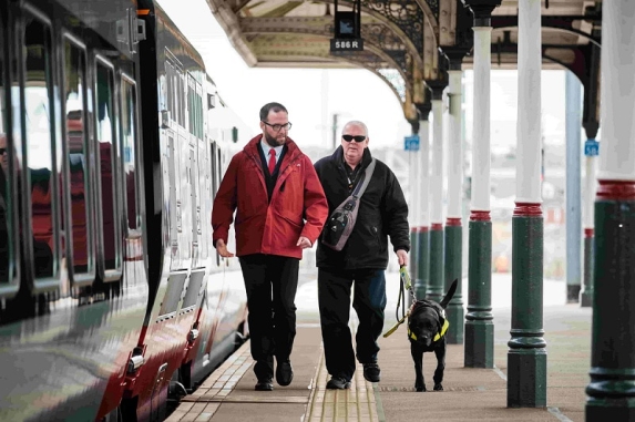 Member of staff walking with blind man and dog 