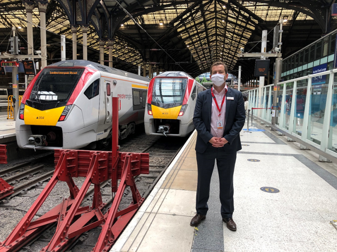 Man wearing a face covering whilst standing in front of trains