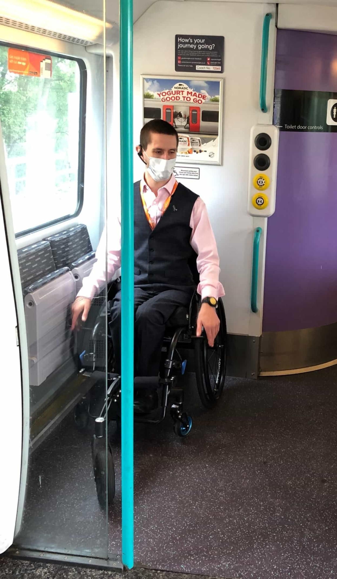 Man wearing a blue face covering sitting in wheelchair on a train