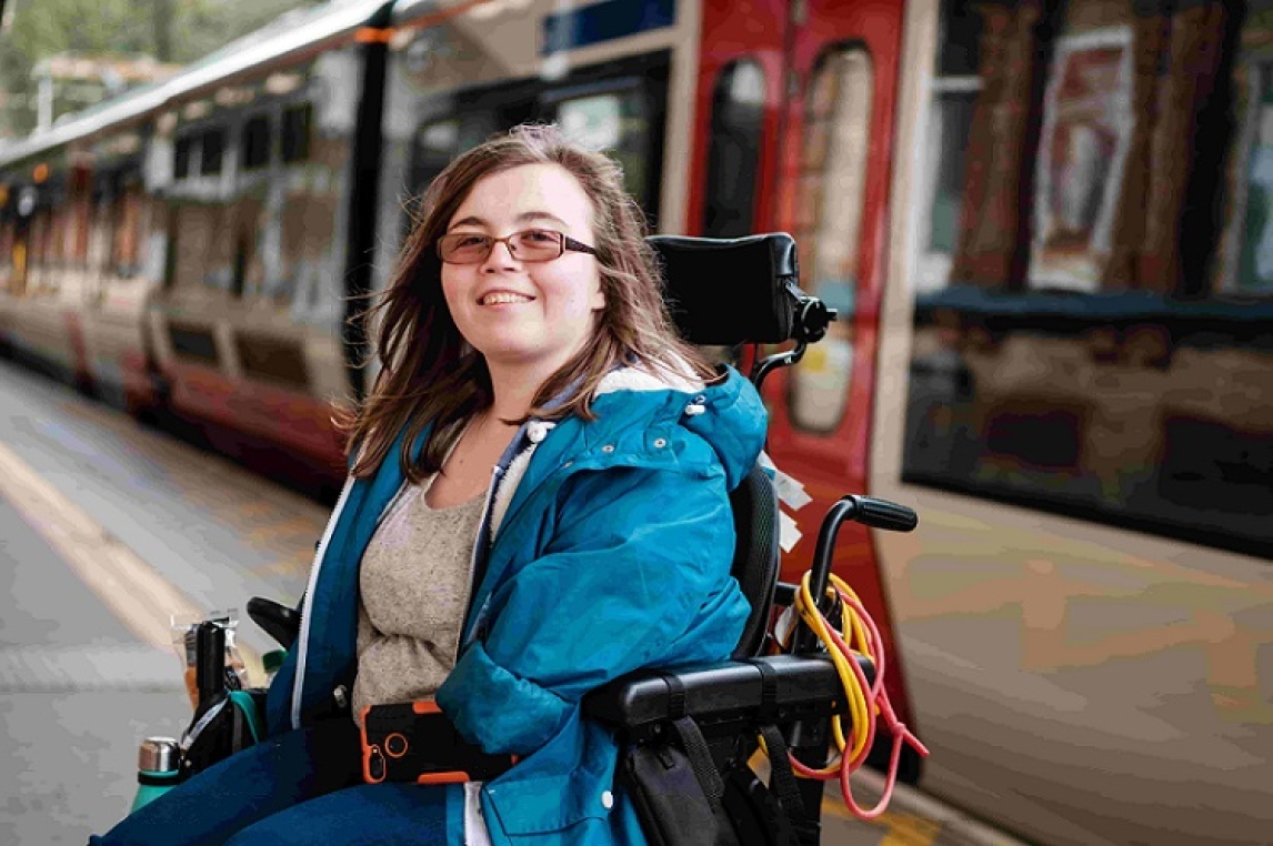 Disabled woman in a wheelchair, smiling at camera with a train in the background